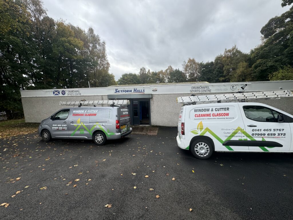 Two service vans parked outside a white commercial building with signage for various services.