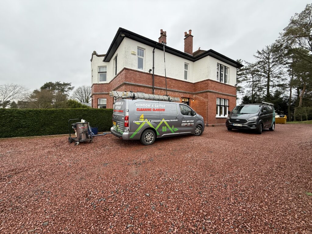 A residential house with two branded service vans parked outside on a red gravel driveway.