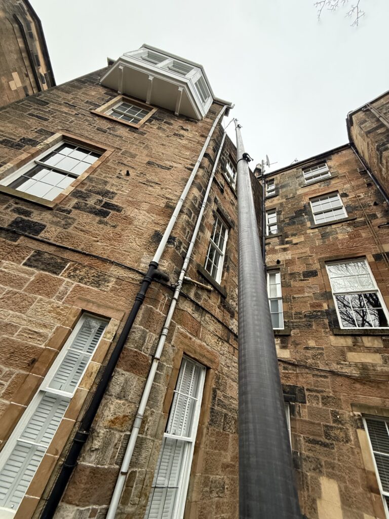 View looking up between two tall old brick buildings with pipes and windows.