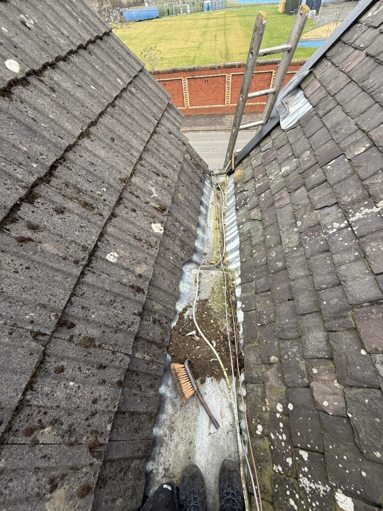 A narrow roof valley filled with debris and leaves.